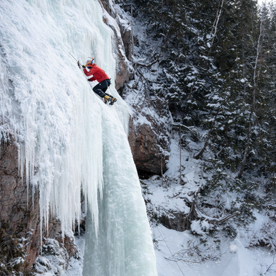 Person ice climbing a frozen waterfall in a snowy forest